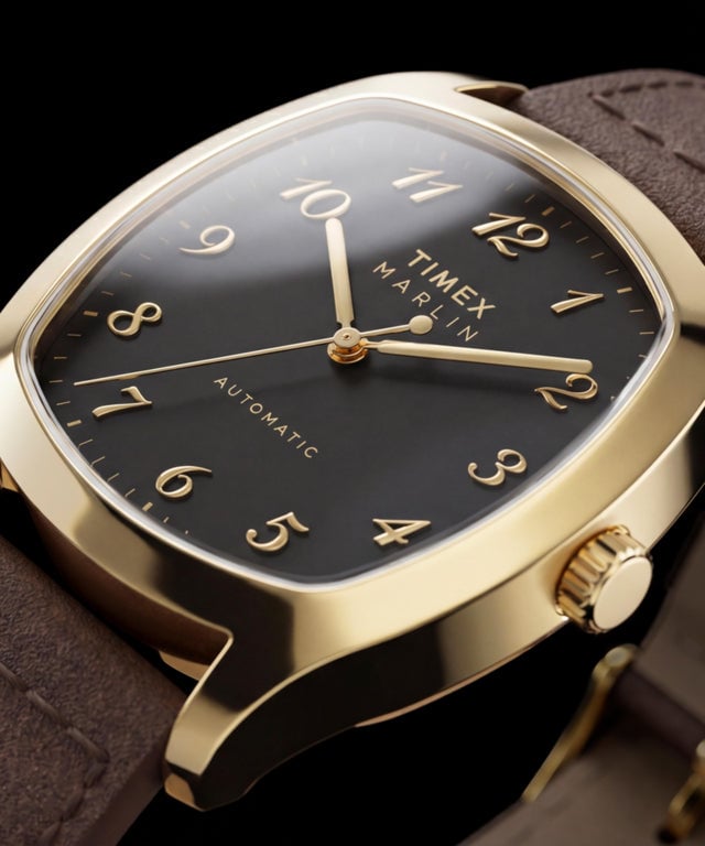 金色 Timex Marlin Chatham Automatic 的特写,展示其黑色表盘、金色立体阿拉伯数字时标、金色指针和棕色皮革表带