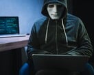一个戴着面具和兜帽的人在昏暗的房间里使用笔记本电脑。