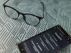 一款智能手机上打开了ChatGPT应用，旁边是一副眼镜，背景为带图案的表面