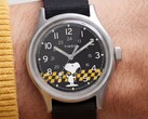 Timex MK1黑色表盘的特写镜头，表盘上以黄黑格纹为背景印有史努比图案，配有阿拉伯数字时标和夜光指针。