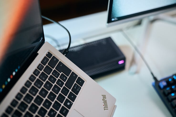 一张特写照片,展示了一根 Thunderbolt 5 数据线插入联想 ThinkPad X9 笔记本电脑侧面接口的情景,背景中可见 Aorus 外置显卡。