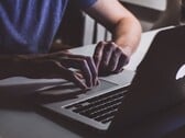 在微弱的光线下，一双双手正在MacBook键盘上敲击，苹果标志正发出微光