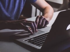 在微弱的光线下,一双双手正在MacBook键盘上敲击,苹果标志正发出微光