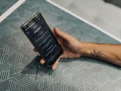 一只手握着智能手机，手机上打开了 ChatGPT 应用，位于带有图案的桌子上方