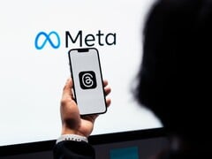 一只手握着智能手机,手机位于一个巨大的 Meta 标志前方