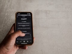 一只手拿着智能手机,屏幕上显示 ChatGPT 界面,背景是灰色石质表面