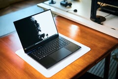 一台深黑色Razer Blade 16游戏笔记本电脑，置于白色桌垫上，桌垫下是温暖的木质桌面，屏幕上显示着一幅生动鲜明的黑白壁纸。