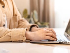 一双双手正在明亮的书桌上,通过打开的笔记本电脑键盘进行打字