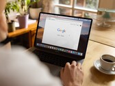 一名用户坐在笔记本电脑前，屏幕上打开着 Google 主页，旁边放着一杯咖啡