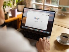 一名用户坐在笔记本电脑前，屏幕上打开着 Google 主页，旁边放着一杯咖啡