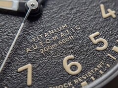Timex Expedition Field Post Titanium 腕表的特写镜头，展现其带有阿拉伯数字的纹理黑色表盘、夜光指针和时标，以及日期窗口。