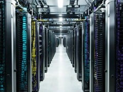 高密度计算大厅内一排排 Meta 数据中心服务器机架，上面有彩色编码的电缆和架空电源系统。(图片来源：Meta）