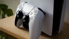 一张 PlayStation 5 DualSense 控制器斜靠在 PS5 主机上的图片