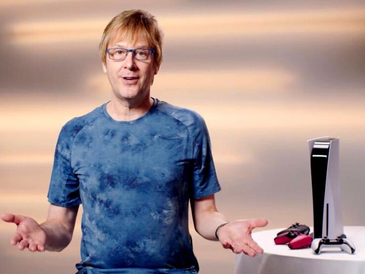 马克-切尼（Mark Cerny）在一次 PlayStation 活动中，坐在 PS5 游戏机和 DualSense 控制器旁。(图片来源：索尼互动娱乐公司）