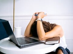 一名女子低头看着智能手机，身旁放着一台笔记本电脑