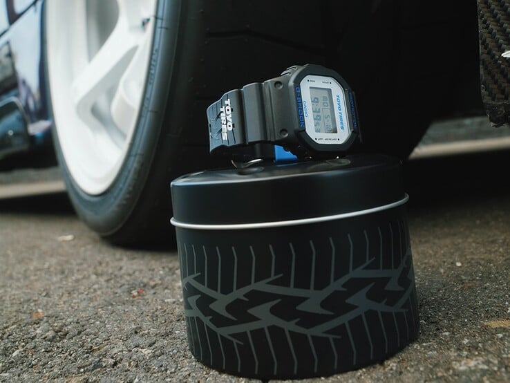 卡西欧G-Shock DW5600TT25-1 x 东洋轮胎联名款手表陈列在一个以轮胎为主题的金属罐上,旁边放着一个汽车轮毂。