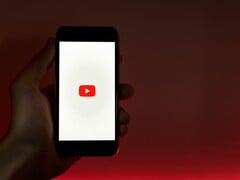 一只手握着智能手机，屏幕上亮着YouTube标志，背景为红色