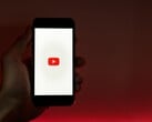 一只手握着智能手机，屏幕上亮着YouTube标志，背景为红色