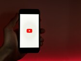 一只手握着智能手机，屏幕上亮着YouTube标志，背景为红色