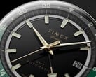Timex Atelier GMT Première M1a 黑色表盘特写，配有金色指针、夜光时标、日期窗，以及黑绿双色 24 小时 GMT 表圈。