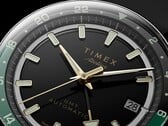 Timex Atelier GMT Première M1a 黑色表盘特写，配有金色指针、夜光时标、日期窗，以及黑绿双色 24 小时 GMT 表圈。