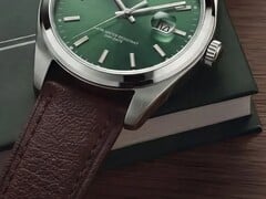 Timex Legacy Day and Date 腕表特写,展示其绿色太阳纹表盘、银色表圈和拉丝表耳、带凹槽的表冠以及纹理棕色皮革表带,背景为深绿色盒子和木质表面。