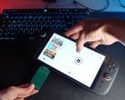 来自 YouTube 频道 Better Gaming 的 Yu 一手拿着任天堂 Switch 2，一手拿着开源绿色 PCB 适配器，试图将其插入设备的 microSD Express 插槽（图片来源：Better Gaming via YouTube）