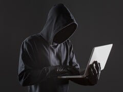 一个戴着头罩的黑客在黑暗的背景下操作着一台笔记本电脑。