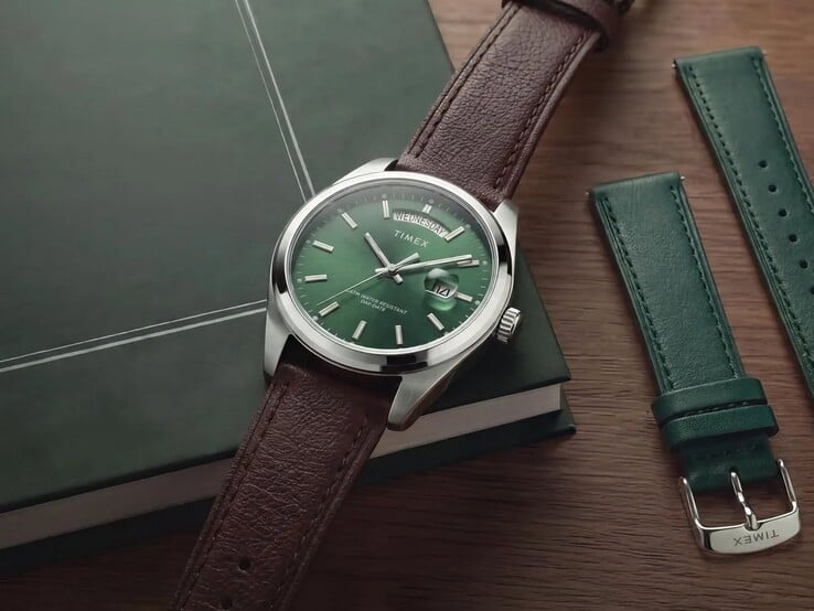 绿色表盘、棕色皮革表带的 Timex Legacy Day and Date 腕表陈列在一本深绿色的书上,旁边放着可替换的绿色皮革表带。
