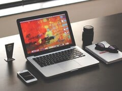 深色桌面上的 MacBook Pro,旁边放着智能手机、眼镜和笔记本。