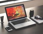 深色桌面上的 MacBook Pro,旁边放着智能手机、眼镜和笔记本。