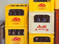黄白相间的塑料箱堆满了朝日啤酒瓶，上面印有日文和红色标识。(图片来源：Alazne Lazcano 通过 Pexels 提供的照片）