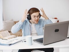 一名戴着耳机的男子在笔记本电脑前沮丧地举起双手