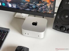 一台搭载 Apple M6 处理器的 Mac mini 置于游戏设置的桌面上，配有显示器、键盘、鼠标和扬声器。