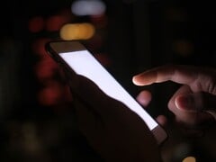 一只手在黑暗中握着一部屏幕发光的智能手机