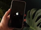 一只手握着一部iPhone，屏幕上显示着苹果标志和进度条。