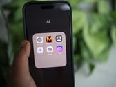 一只手拿着一部智能手机，屏幕上显示着一个名为“AI”的文件夹，其中包含 Gemini、ChatGPT 和 Claude 等应用程序