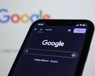 智能手机显示 Google 搜索页面,背后是一块带有 Google 标志的屏幕