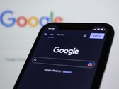 智能手机显示 Google 搜索页面，背后是一块带有 Google 标志的屏幕