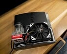 定制水冷式 PlayStation 3,配有红色 SysCooling 泵和安装在机箱内的大型黑色风扇,放置在木桌上。 图片来源:Zac Builds via YouTube