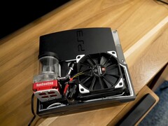 定制水冷式 PlayStation 3,配有红色 SysCooling 泵和安装在机箱内的大型黑色风扇,放置在木桌上。 图片来源:Zac Builds via YouTube
