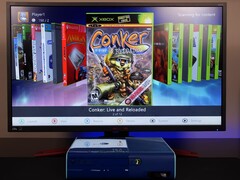一台经过改装的蓝色 Xbox 360 在显示器上运行自定义自制仪表盘，显示游戏 &quot;Conker：Live and Reloaded &quot;以及其他 Xbox 和模拟器游戏。(图片来源：YouTube 上的 Modern Vintage Gamer）