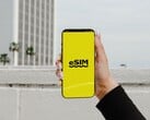 一只手拿着智能手机,黄色屏幕上醒目地显示着“eSIM”字样。