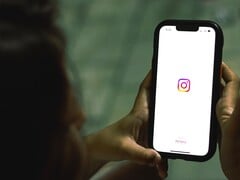一名女子双手捧着智能手机,屏幕上显示的是 Instagram 的首页