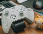 白色的 Xbox 控制器放在木质书桌上，旁边摆着一只小猫公仔（图片来源：FOX ^.ᆽ.^= ∫ via Pexels）