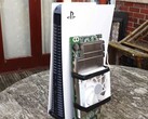 一台 PlayStation 5 游戏机放置在一块定制的 AMD BC250 电路板旁边，该电路板安装有散热片和冷却风扇。(图片来源：Budget-Builds Official via YouTube）
