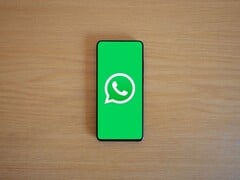 一张木质桌子上放着一部智能手机,屏幕显示着带有WhatsApp标志的绿色启动界面。