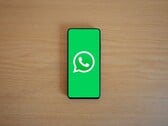一张木质桌子上放着一部智能手机，屏幕显示着带有WhatsApp标志的绿色启动界面。